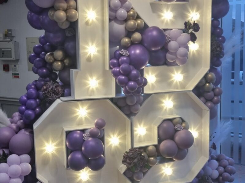 Light Up letters for the year 1982 surrounded by purple and lilac balloons
