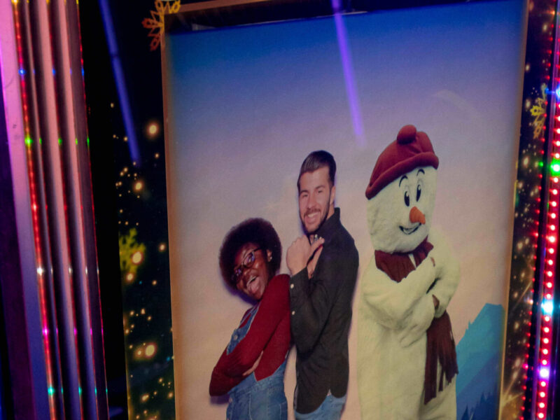 Two party goers see their picture on the screen with a snowman stood next to them