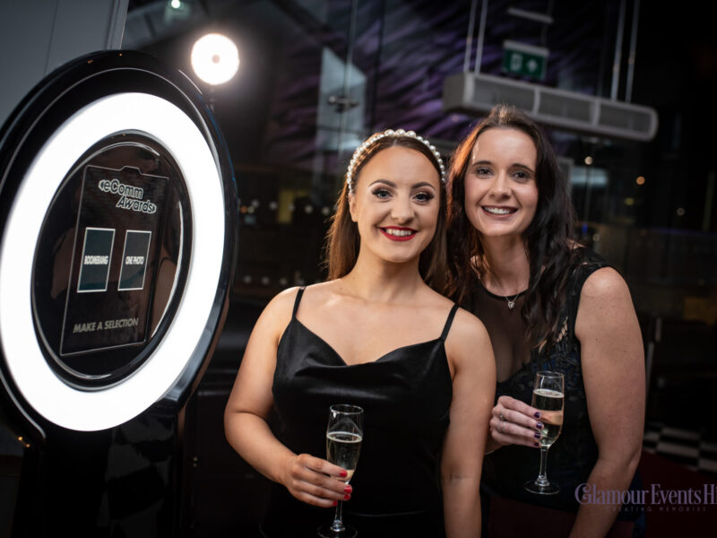 Two pretty ladies having fun at an event, drinking champagne and posing to have their photos taken on the Pylon