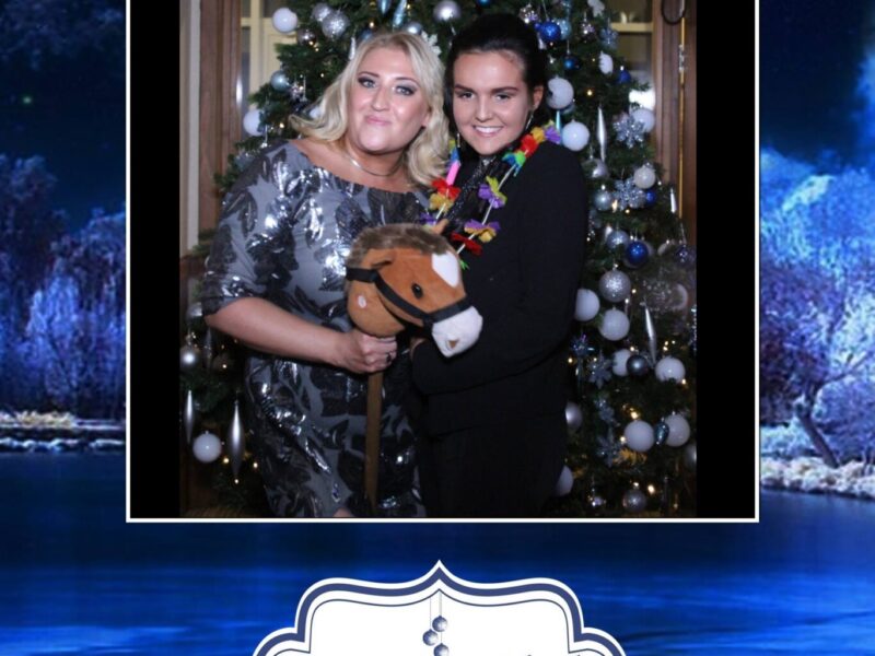 Picture of two women at a party in front of a Christmas tree holding props and having fun.