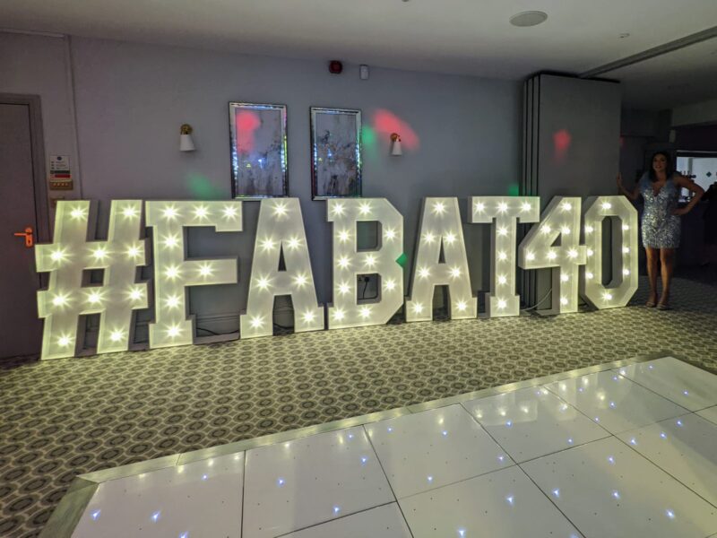 Light up letters are shown reading #FABAT40. A White LED dancefllor is in front of them in a function room. There is a beautiful birthday girl stood at the end of them.